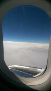 Underwater Scooter Adventures - an inside view looking out a plane window, over the wing, at a blue sky above the white clouds