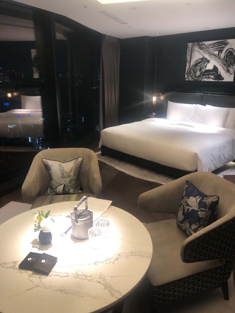 Local Secrets Edition 4: The Penthouse In The Sky. Image of the Deluxe King Room in the Bellustar Hotel Tokyo with marble coffee table with two chairs on either side, ice bucket and glasses, and king bed in the background.