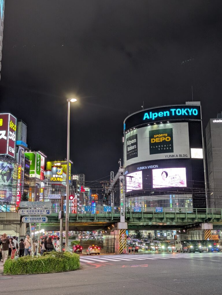 Local Secrets Edition 4: The Penthouse In The Sky. Image of neo-lit streets of Shinjuku Tokyo with Alpen Tokyo retail store and billboards in the background.