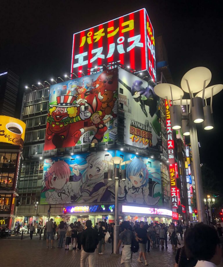 Local Secrets Edition 4: The Penthouse In The Sky. Image of one of Shinjuku neon-lit streets with people everywhere and anime billboards as the backdrop